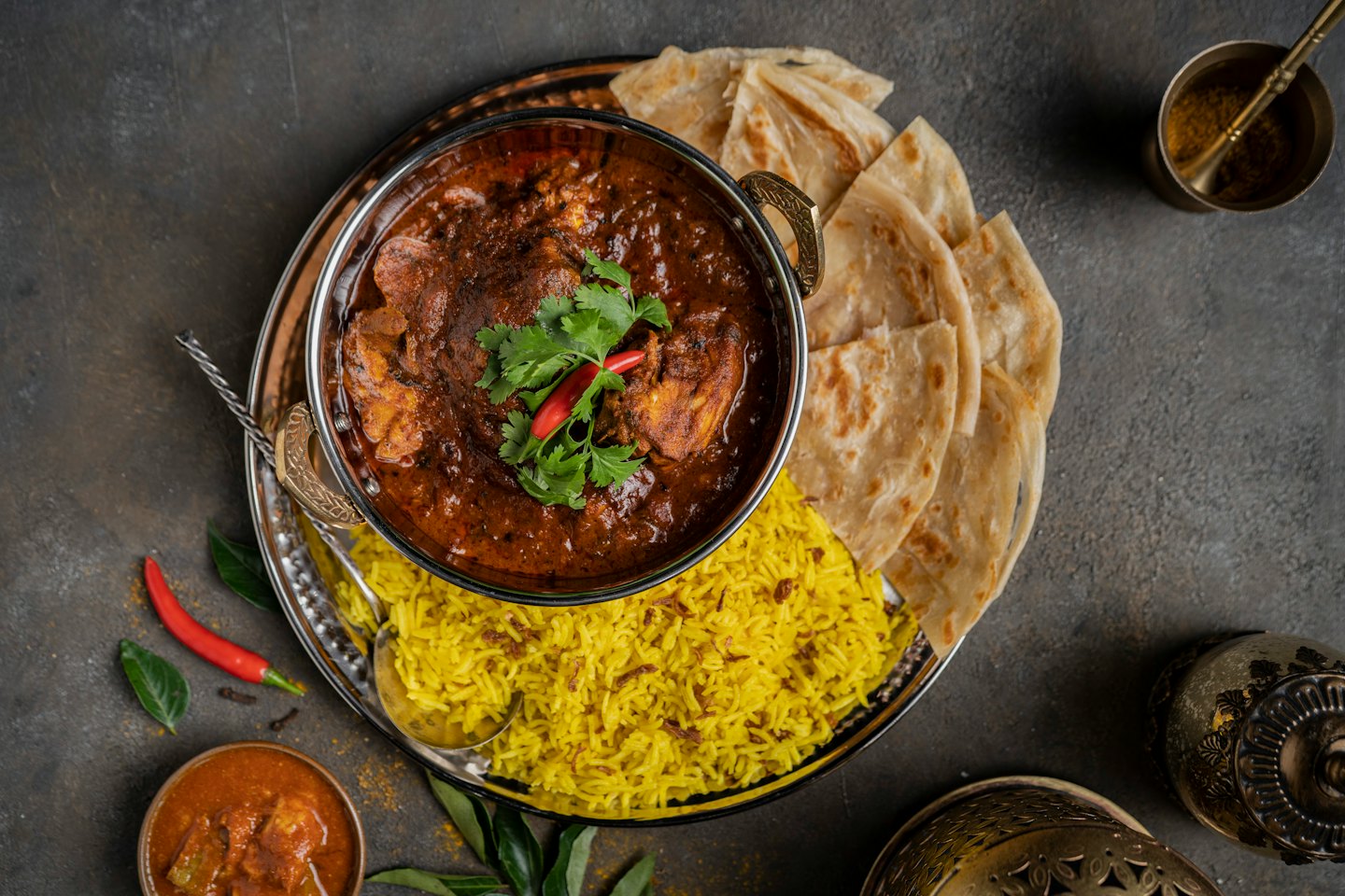 Chicken curry served in a metallic bowl with rice and flatbread.
