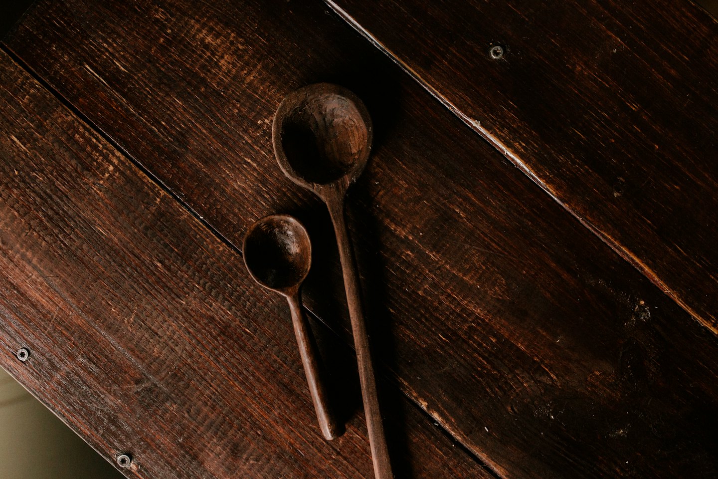 Two hand-carved wooden spoons on a rustic wooden surface.