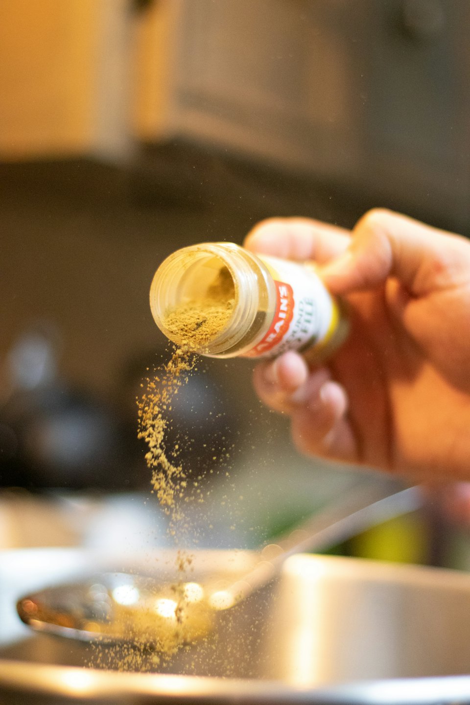 Hand shaking powdered spice from a jar into a bowl.